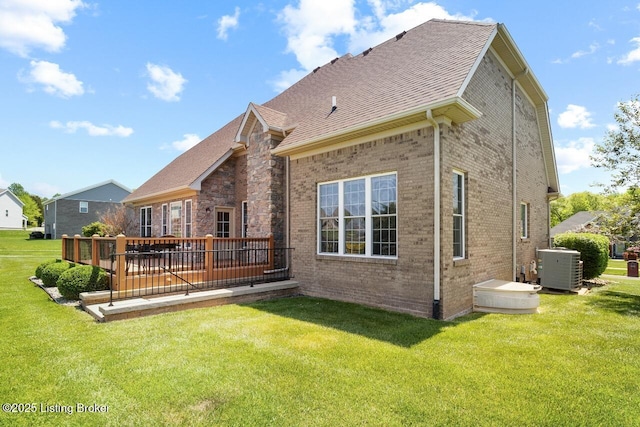 rear view of house featuring a yard, brick siding, central AC, a deck, and roof with shingles