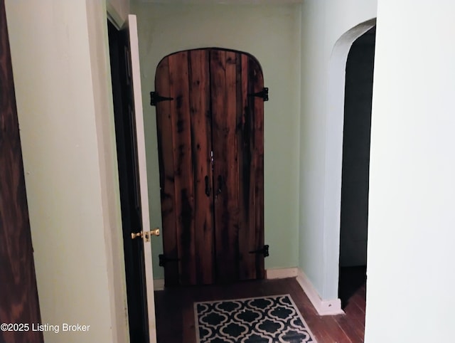 hall featuring arched walkways, baseboards, and dark wood-style floors