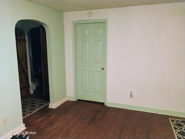 spare room with dark wood finished floors, arched walkways, and baseboards