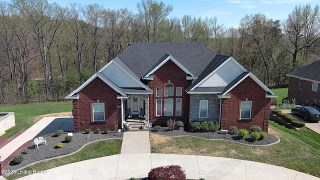 traditional home featuring brick siding, a wooded view, a shingled roof, and a front yard