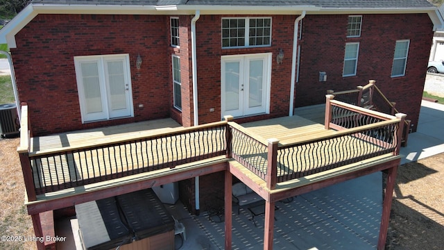 rear view of house with central AC unit, french doors, a wooden deck, brick siding, and roof with shingles