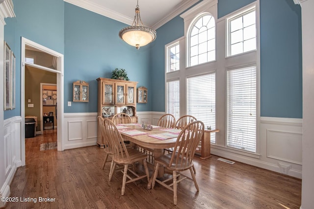 dining room featuring wainscoting, visible vents, a towering ceiling, wood finished floors, and crown molding
