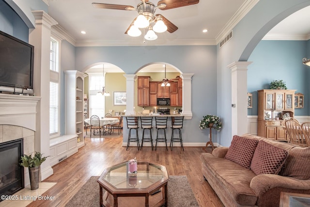 living room with crown molding, a ceiling fan, light wood-type flooring, a tile fireplace, and visible vents