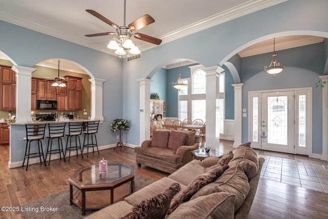 living room with wood finished floors, ornamental molding, ceiling fan, and decorative columns