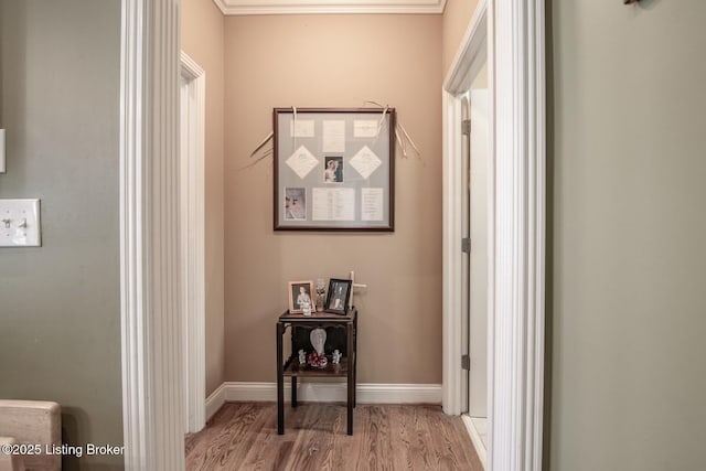 corridor with light wood finished floors, baseboards, and ornamental molding