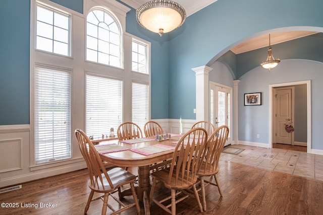 dining space featuring decorative columns, visible vents, a healthy amount of sunlight, arched walkways, and wainscoting