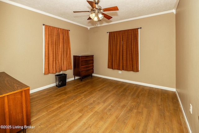 empty room with crown molding, ceiling fan, baseboards, and wood finished floors
