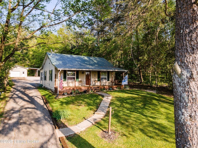 view of front of house with covered porch, metal roof, a front yard, an outbuilding, and a garage