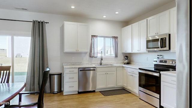 kitchen featuring a sink, light wood-style floors, stainless steel appliances, light countertops, and white cabinets