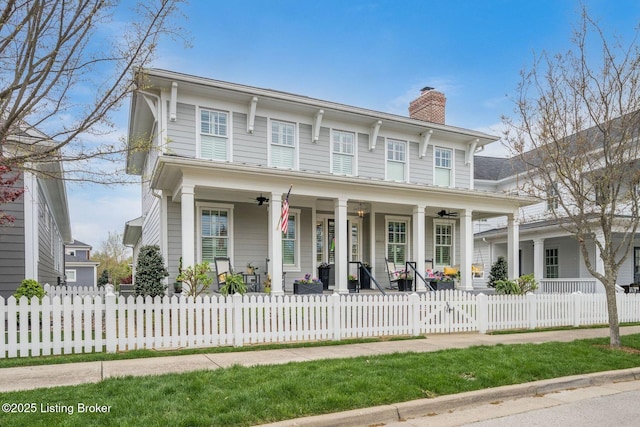 italianate-style house featuring a chimney, a porch, ceiling fan, and a fenced front yard