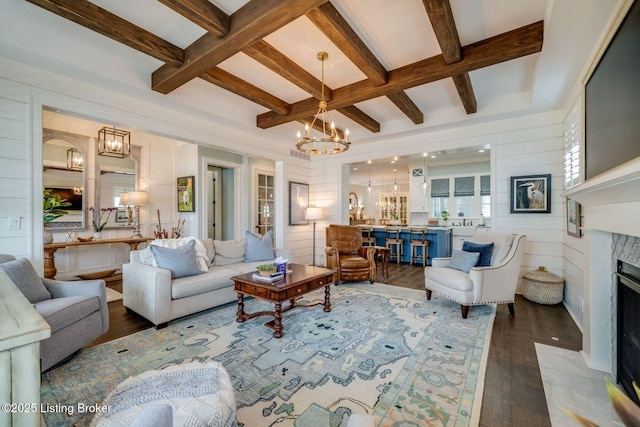 living room with coffered ceiling, an inviting chandelier, a high end fireplace, wood finished floors, and beam ceiling