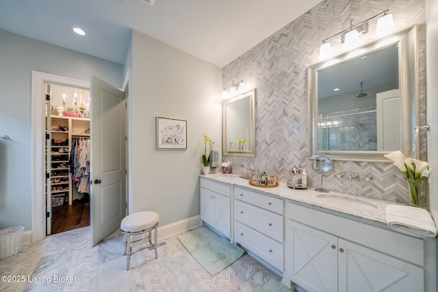 bathroom with a sink, a walk in closet, double vanity, baseboards, and tiled shower