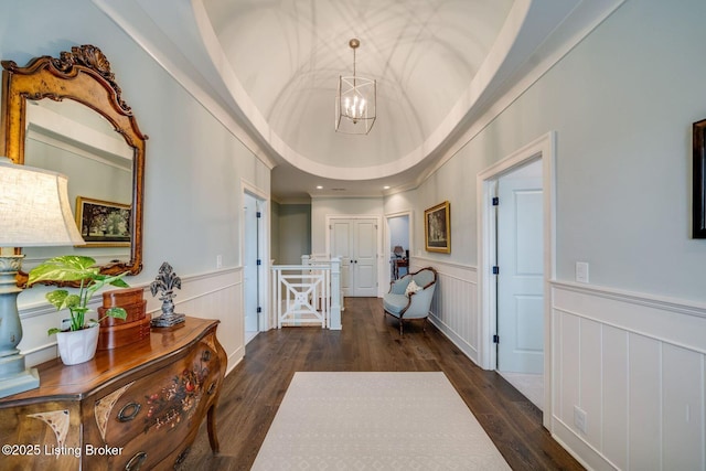 hallway with wood finished floors, a decorative wall, a wainscoted wall, and a chandelier