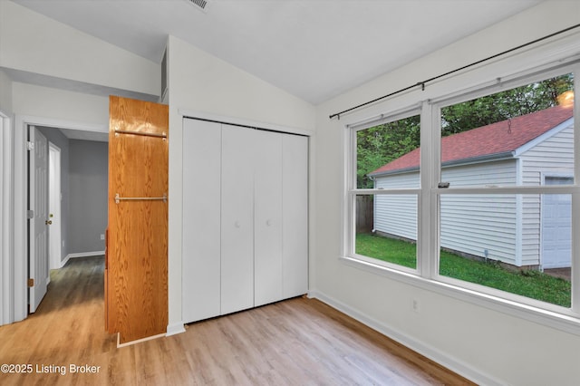 unfurnished bedroom with lofted ceiling, baseboards, light wood finished floors, and a closet