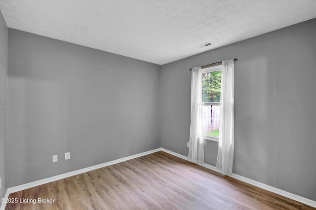 unfurnished room featuring baseboards, wood finished floors, visible vents, and a textured ceiling