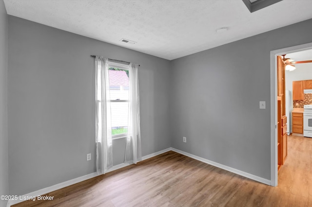 spare room featuring light wood finished floors, plenty of natural light, baseboards, and visible vents
