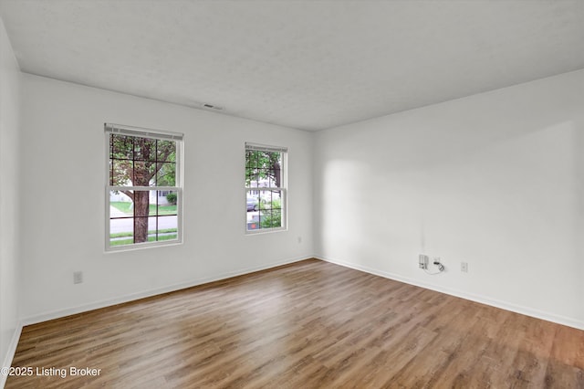 spare room featuring wood finished floors, visible vents, and baseboards