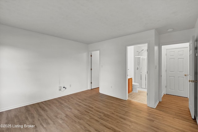unfurnished bedroom featuring ensuite bathroom, baseboards, and light wood-style floors