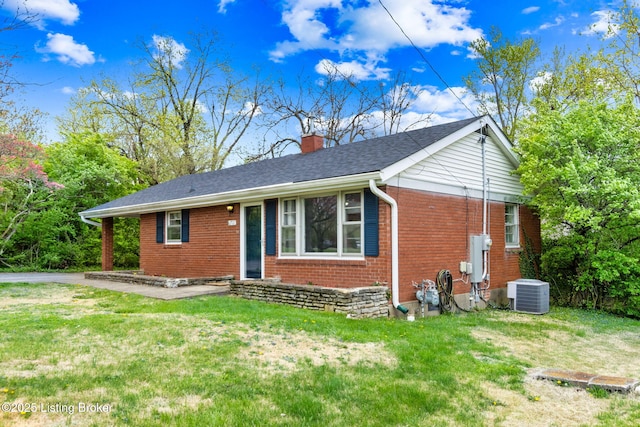 ranch-style house featuring a front lawn, a chimney, brick siding, and central air condition unit