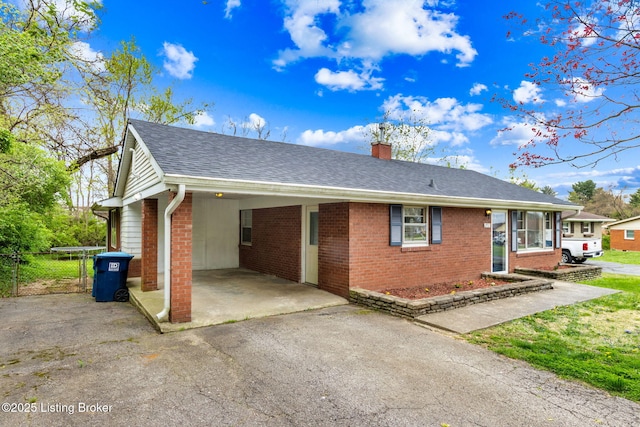 single story home featuring a chimney, aphalt driveway, a carport, brick siding, and roof with shingles