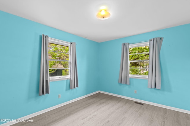empty room with wood finished floors, visible vents, and a healthy amount of sunlight