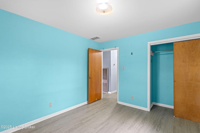 unfurnished bedroom with baseboards, wood finished floors, visible vents, and a closet