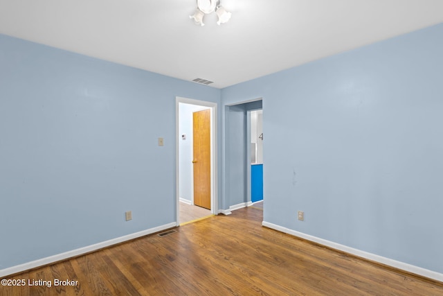 unfurnished room with baseboards, wood finished floors, and visible vents