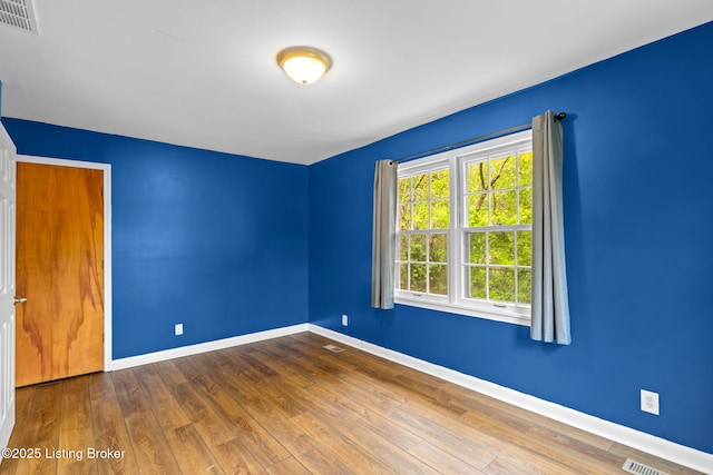 empty room with baseboards, hardwood / wood-style floors, and visible vents