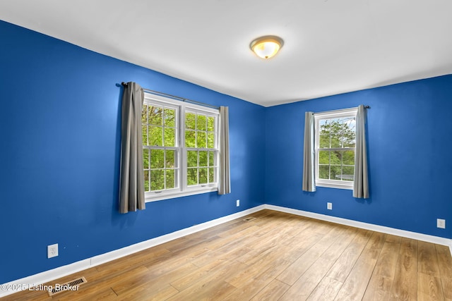 empty room with visible vents, plenty of natural light, baseboards, and wood finished floors