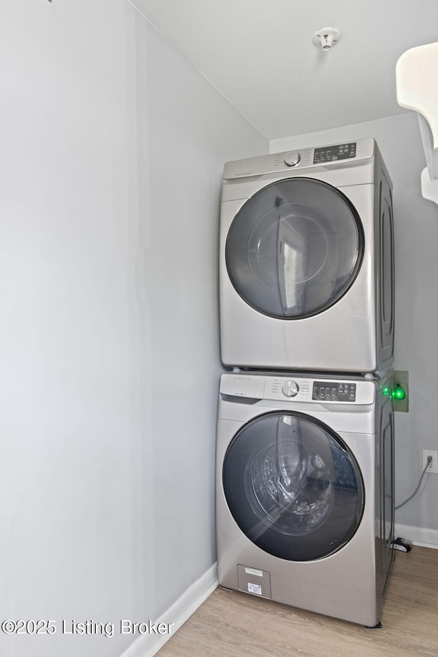 clothes washing area with baseboards, wood finished floors, stacked washer / dryer, and laundry area