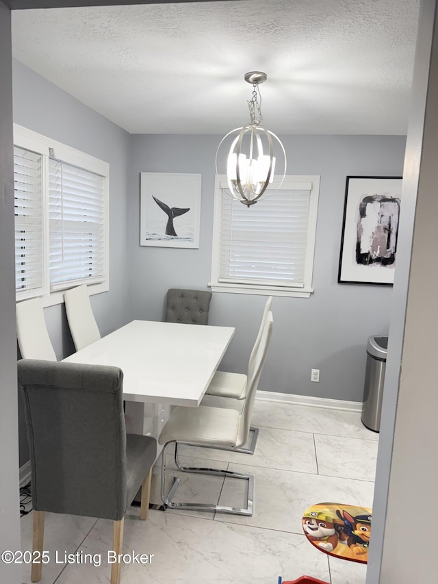 dining area featuring a textured ceiling, marble finish floor, baseboards, and an inviting chandelier