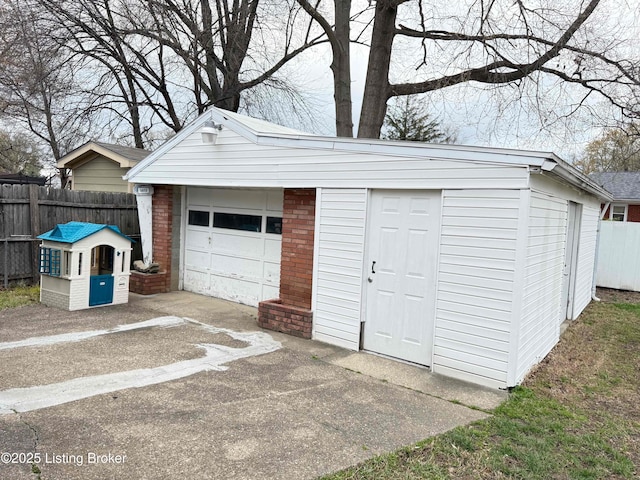 detached garage featuring concrete driveway and fence