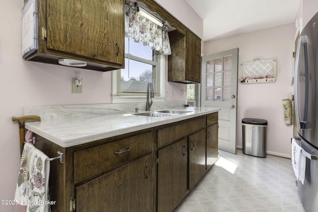 kitchen featuring freestanding refrigerator, baseboards, dark brown cabinets, and a sink