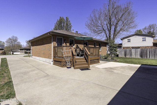 rear view of house with concrete driveway, fence, brick siding, a deck, and a patio