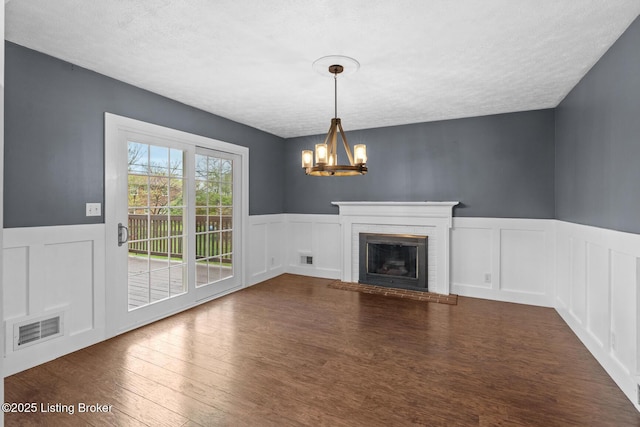 unfurnished living room with visible vents, a decorative wall, wainscoting, a chandelier, and a textured ceiling