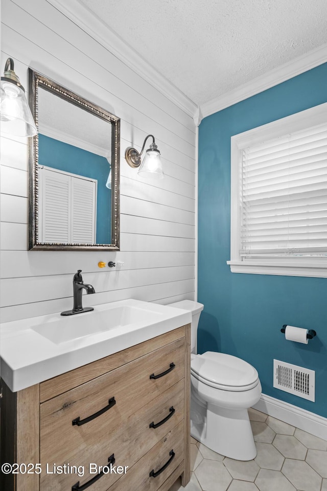 bathroom with crown molding, wood walls, vanity, toilet, and visible vents