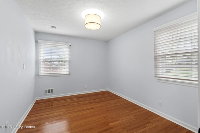 unfurnished room with baseboards, wood finished floors, visible vents, and a textured ceiling
