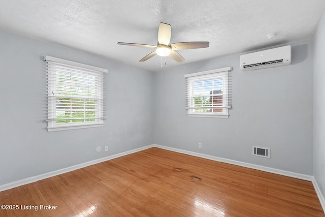 empty room featuring a wall mounted AC, baseboards, visible vents, and a wealth of natural light
