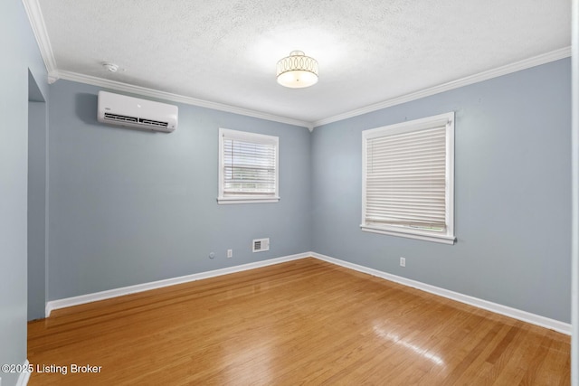 unfurnished room with a textured ceiling, baseboards, a wall mounted air conditioner, wood finished floors, and crown molding