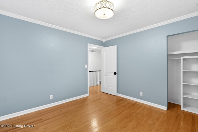 unfurnished bedroom featuring wood finished floors, visible vents, a closet, crown molding, and baseboards