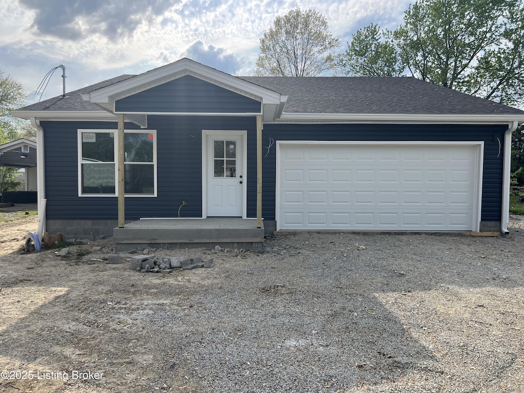 view of front of house featuring dirt driveway, roof with shingles, and a garage