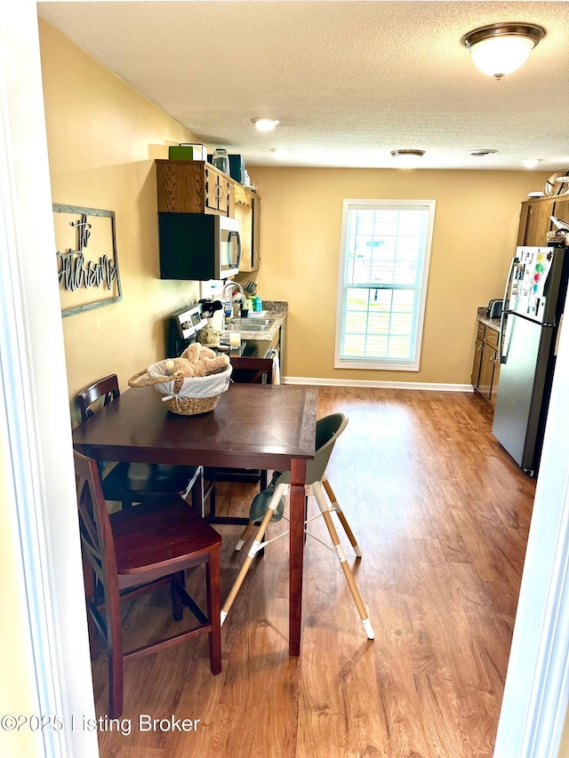 dining area featuring light wood-style flooring, a textured ceiling, and baseboards
