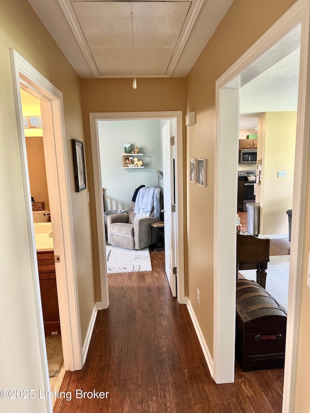 hallway featuring attic access, baseboards, and dark wood-style flooring