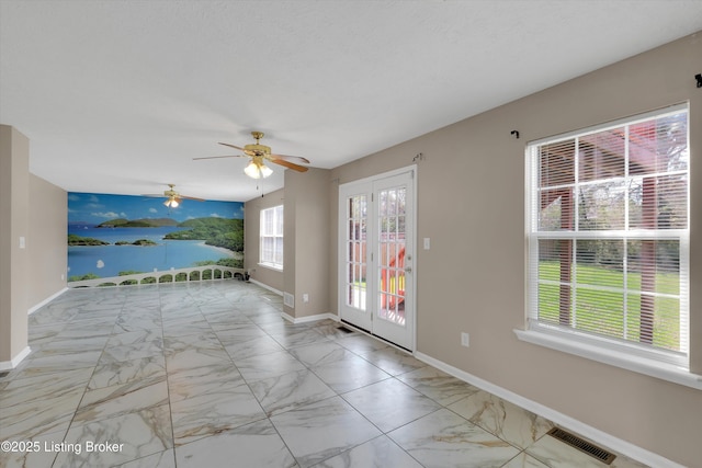 empty room with a water view, ceiling fan, marble finish floor, baseboards, and visible vents