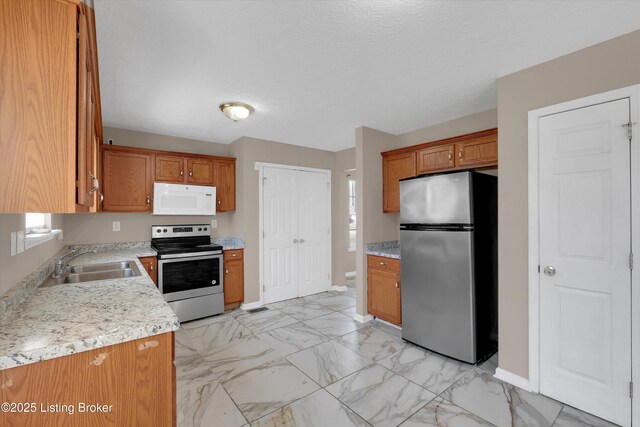 kitchen with a sink, brown cabinets, marble finish floor, light countertops, and appliances with stainless steel finishes