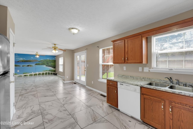 kitchen featuring white dishwasher, a sink, brown cabinetry, ceiling fan, and marble finish floor