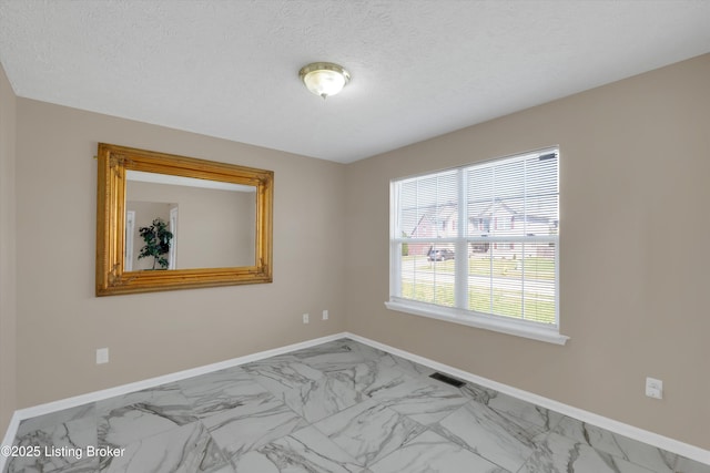 empty room with marble finish floor, baseboards, a textured ceiling, and visible vents