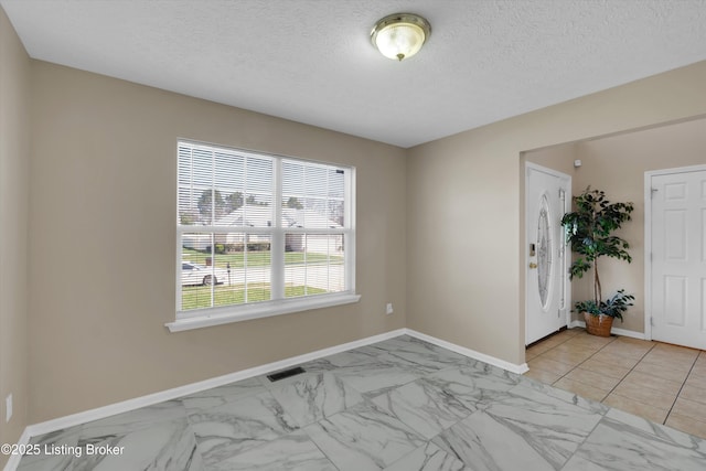 unfurnished room featuring marble finish floor, baseboards, a textured ceiling, and visible vents