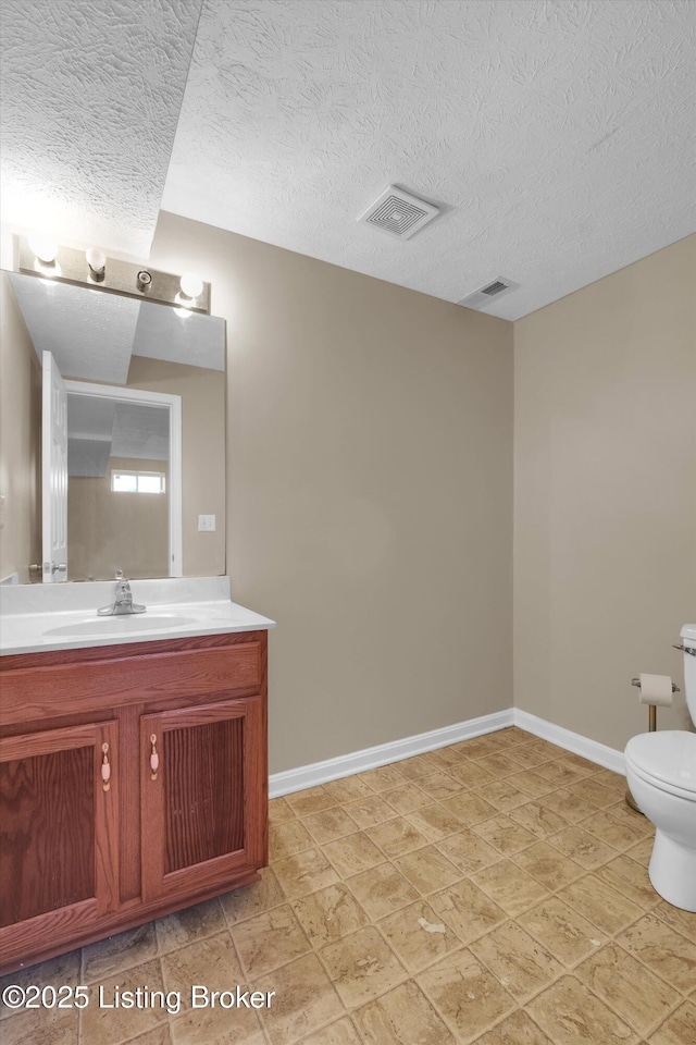 half bath featuring baseboards, visible vents, a textured ceiling, and toilet