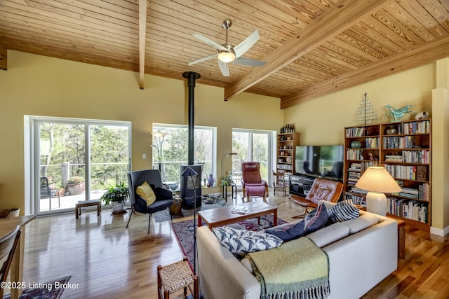 living room with wood ceiling, a wood stove, beam ceiling, and plenty of natural light